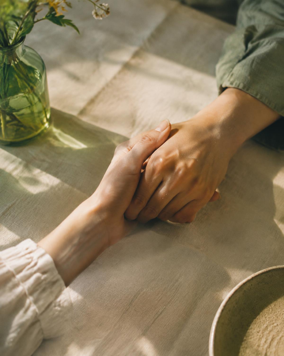 Two hands holding each other on a linen tablecloth